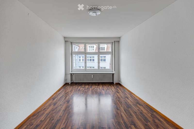 Empty room with wooden flooring, white walls, and large windows with a radiator below. No furniture or equipment present.