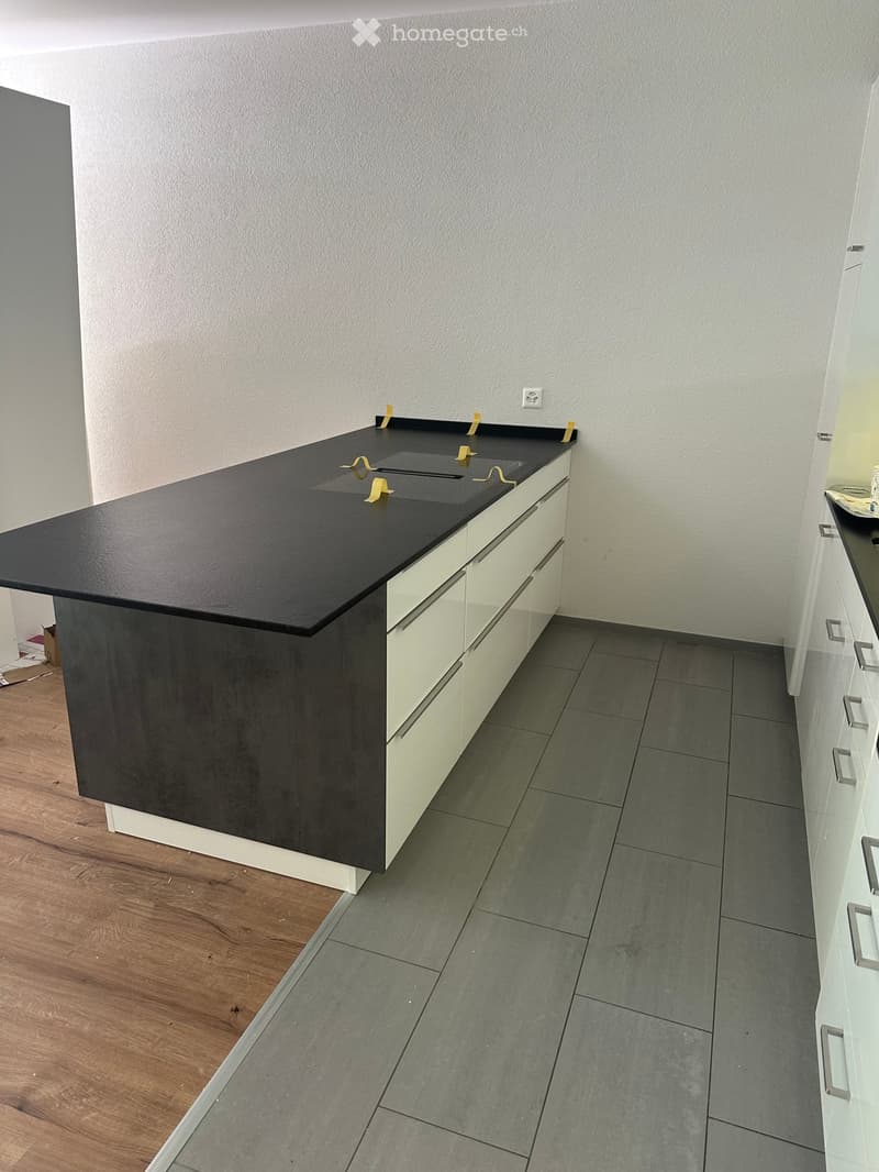 Empty kitchen area with a black countertop, white cabinets, and grey tiled floor. No furniture or appliances are present.