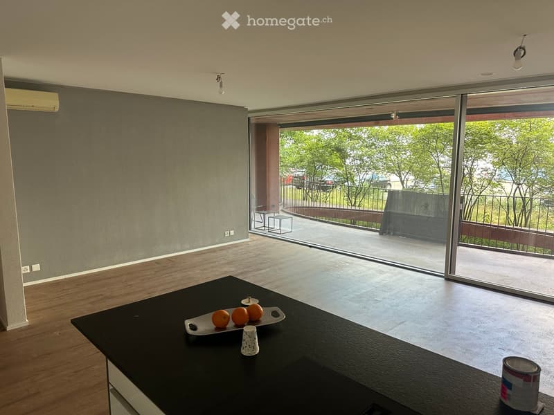 Modern kitchen with wooden flooring, black countertop, and large sliding glass doors leading to a balcony with outdoor furniture.
