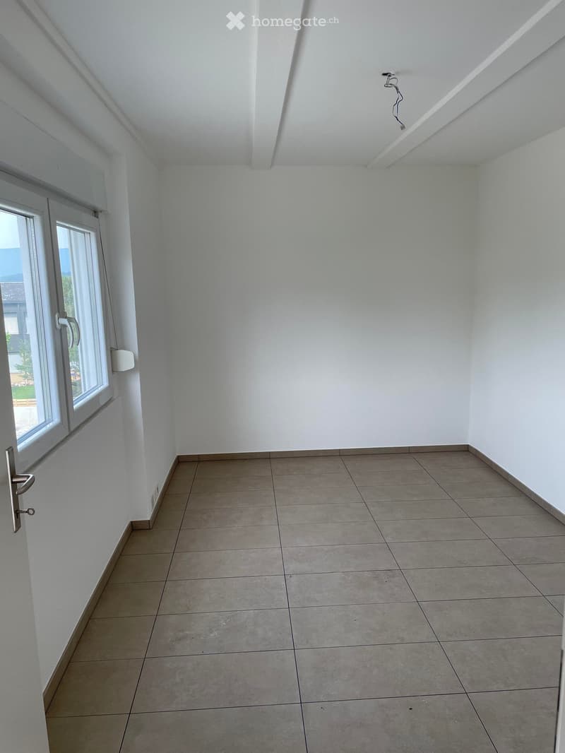 Empty room with white walls, tiled floor, and large window with blinds. No furniture or equipment present.