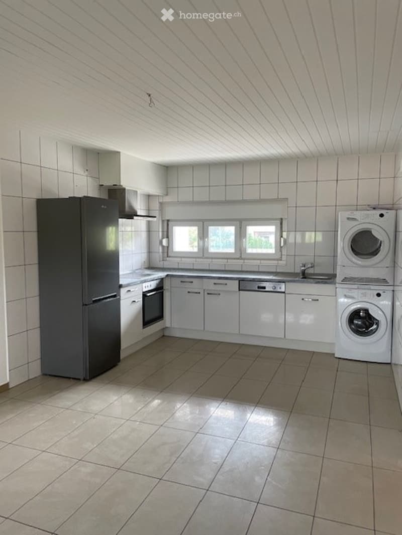 Modern kitchen with white cabinets, stainless steel appliances, and tiled walls and floor. Features a refrigerator, oven, dishwasher, and washing machine.