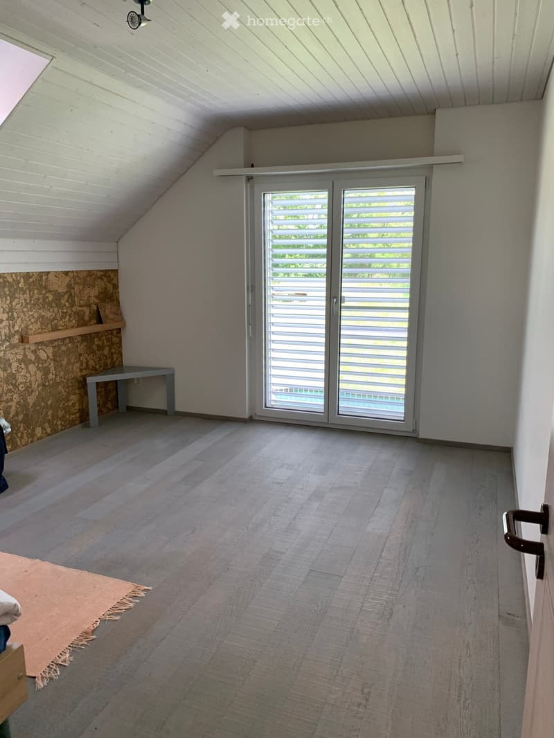 Bright, airy room with wooden flooring, white walls, and a large sliding glass door leading to a pool area. Features a small table and a rug.