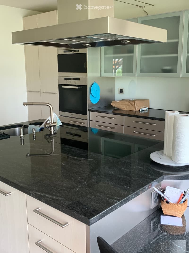 Modern kitchen with black granite countertops, white cabinets, stainless steel oven, and a sleek faucet. Includes a paper towel holder, wicker basket, and various small items on the counter.