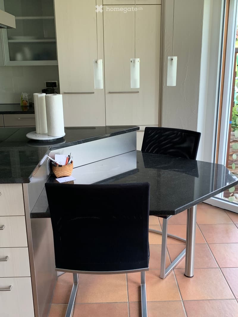 Modern kitchen with light-colored cabinets, black countertop, and a small dining area with two black chairs and a glass table.