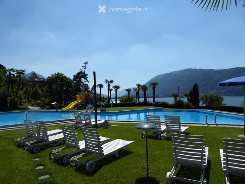 Outdoor area with a swimming pool, lounge chairs, umbrellas, and a view of a lake and mountains.