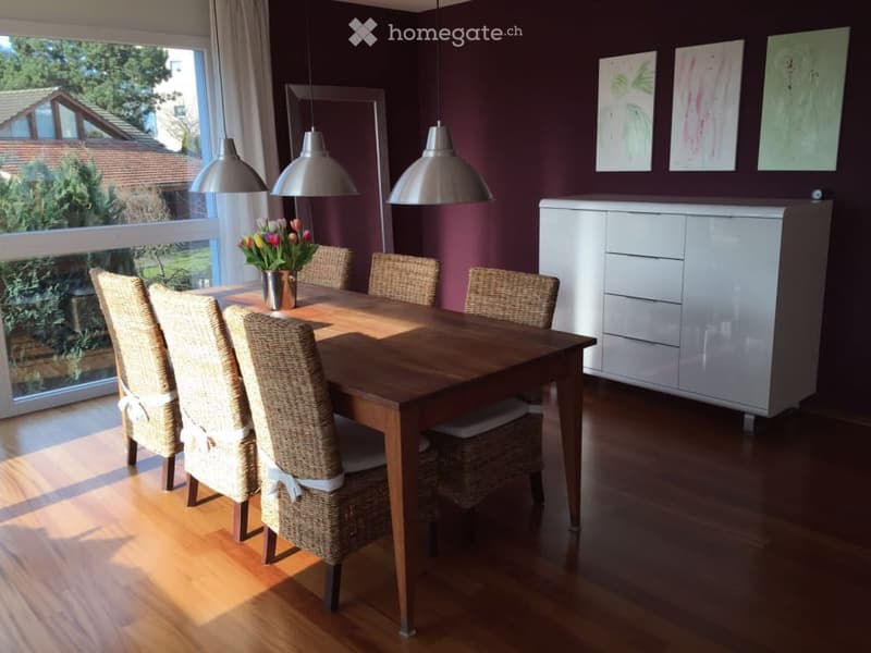 Dining room with a wooden table, wicker chairs, a flower vase, a white cabinet, and pendant lights.