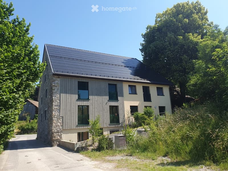 Two-story modern house with a combination of stone and wood exterior, large windows, and a sloped metal roof.