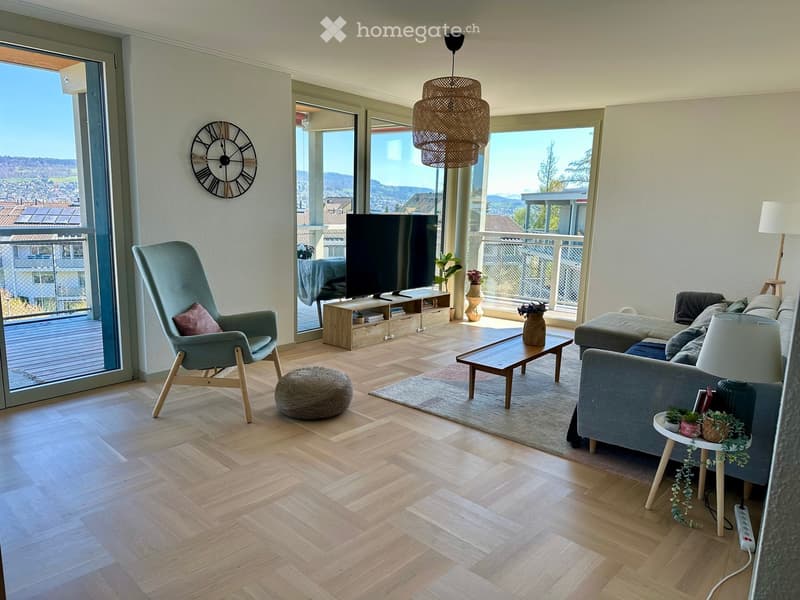 Modern living room with light wooden flooring, large windows offering a scenic view, a grey sofa, a wooden coffee table, a wicker hanging lamp, a TV, and decorative vases.