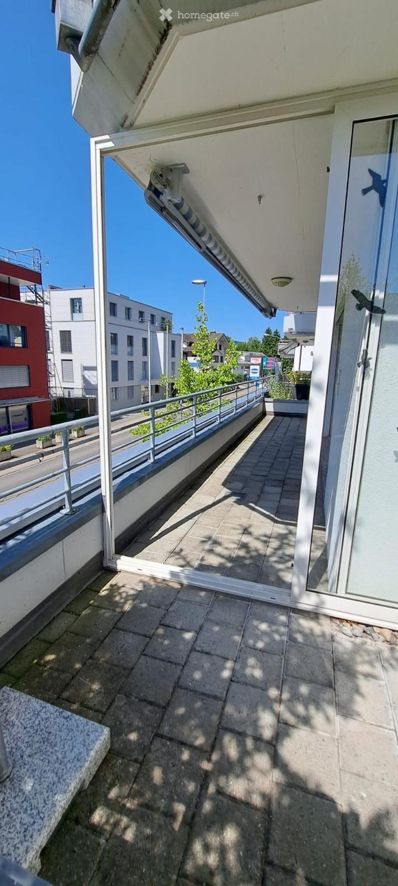Balcony with tiled floor, metal railing, and a view of neighboring buildings and greenery.