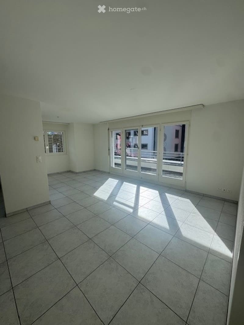 Empty room with sliding glass doors to balcony, white tiled flooring, white walls.