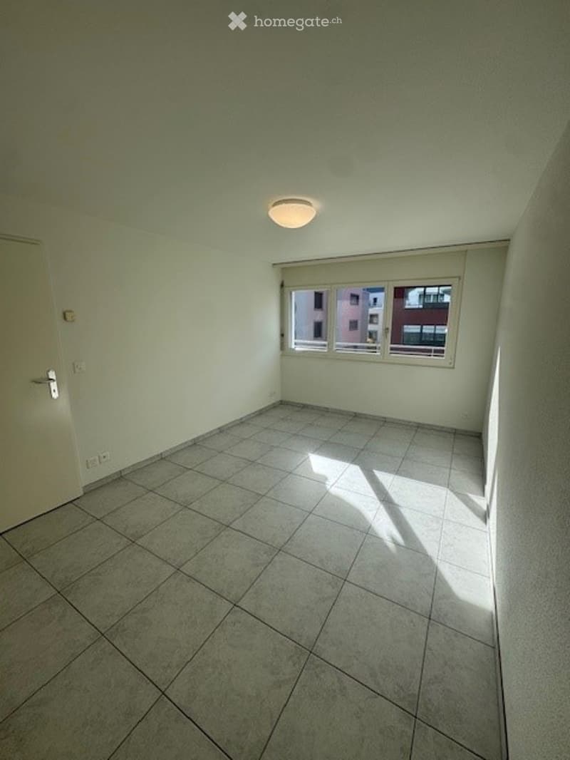 Tiled floor, white walls, large window, overhead lighting, electrical outlets, door