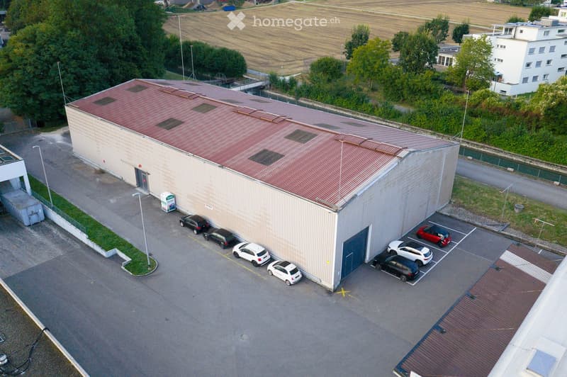 Warehouse, large, multiple parking spots in front, red roof, located in industrial area, adjacent to road, multiple cars parked