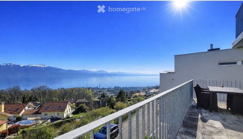 Balcony with a view of a lake and mountains, featuring a table and chairs.