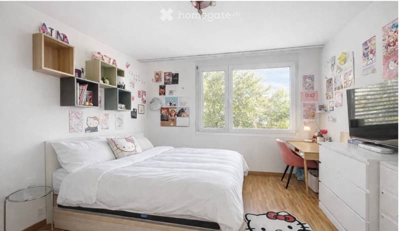 Cozy bedroom with a double bed, wooden desk, chair, nightstand, bookshelf, and a large window with a view of greenery.
