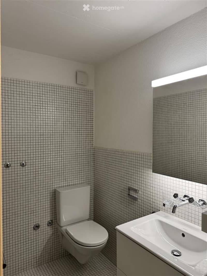 Bathroom. Modern bathroom with white tiled walls, a toilet, a sink with a modern faucet, and a large mirror above the sink.