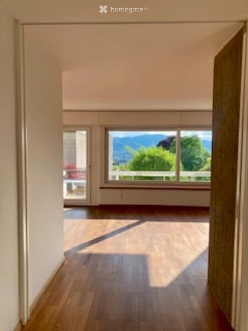 Bright, empty room with wooden flooring and large windows offering a scenic mountain view.