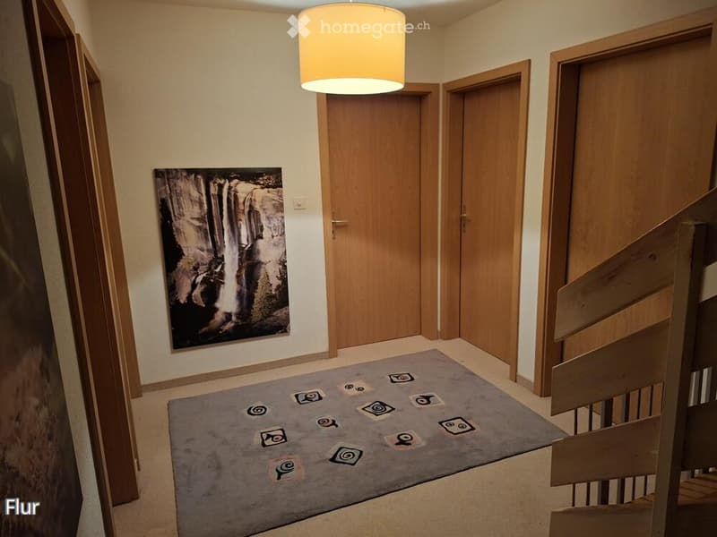 Hallway with wooden doors, a staircase, a round ceiling light, and a grey rug with circular patterns.