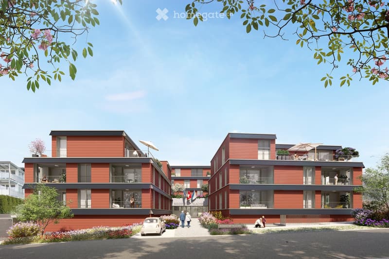 Red building, balconies, entrance with flag, parking area, flower beds, car parked