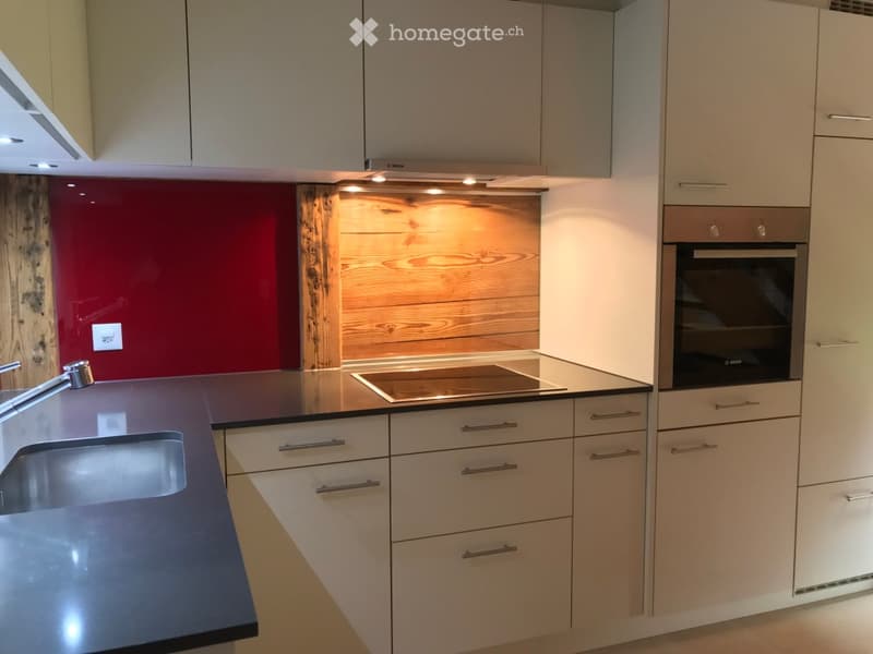 modern kitchen with white cabinets, black countertops, induction stove, oven, sink, faucet, wooden backsplash, red wall