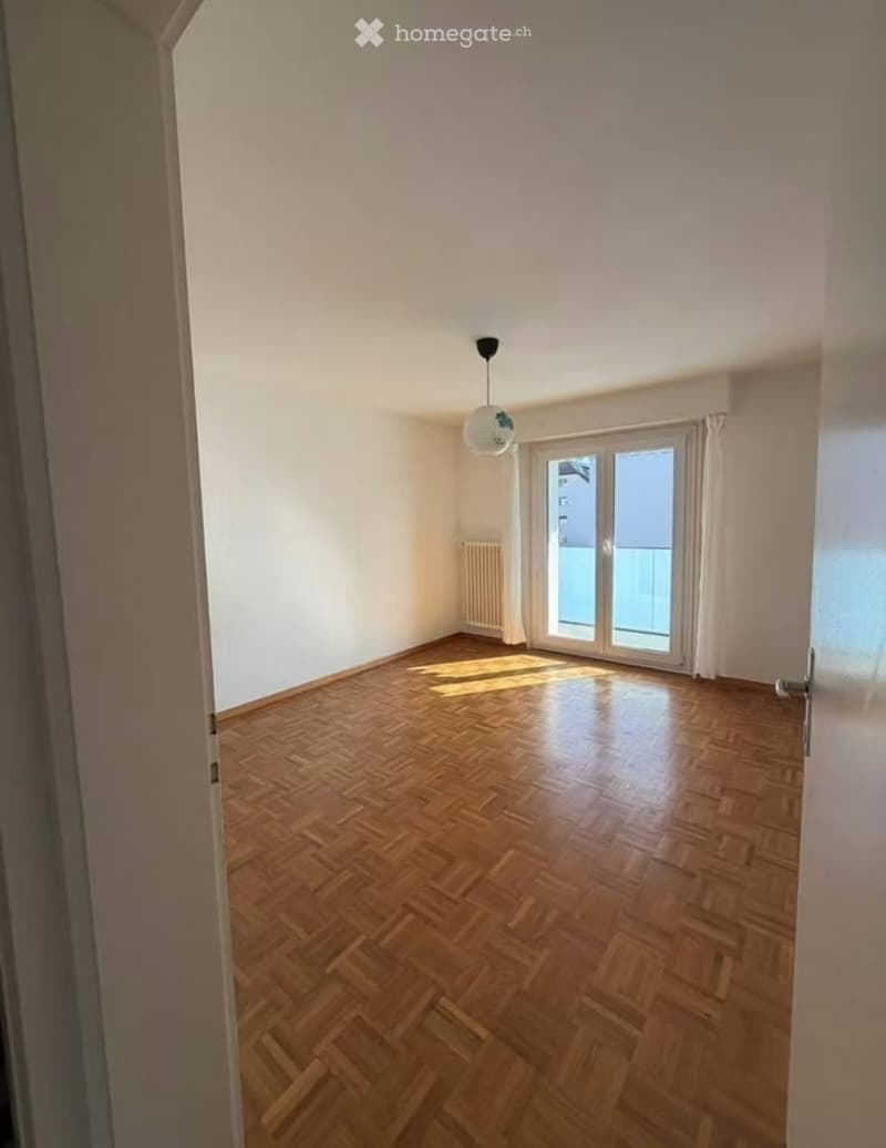 Empty room with wooden parquet flooring, white walls, and large windows leading to a balcony.