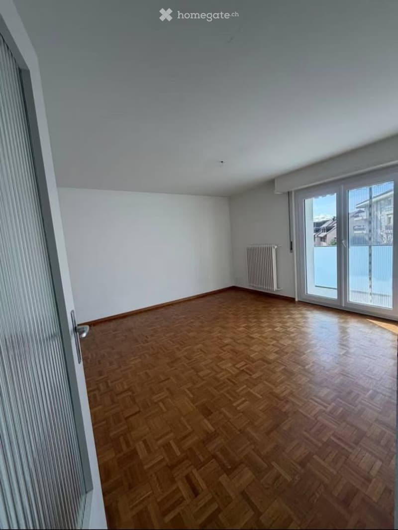 Empty room with wooden parquet flooring, white walls, and large sliding glass doors leading to a balcony.