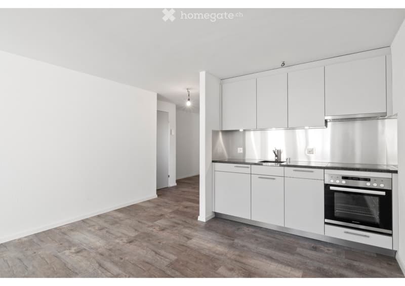 Modern kitchen with white cabinets, stainless steel appliances, and wooden flooring.