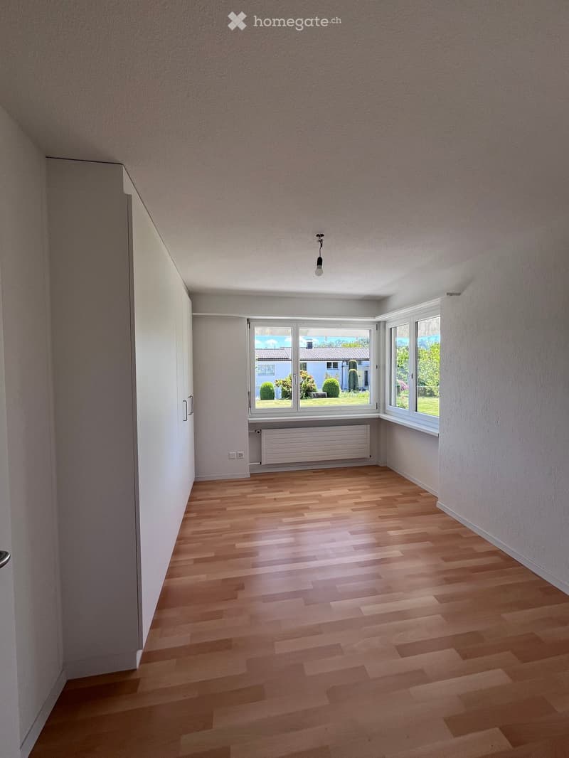 Empty room with wooden flooring, white walls, large windows, and a radiator. No furniture or equipment present.