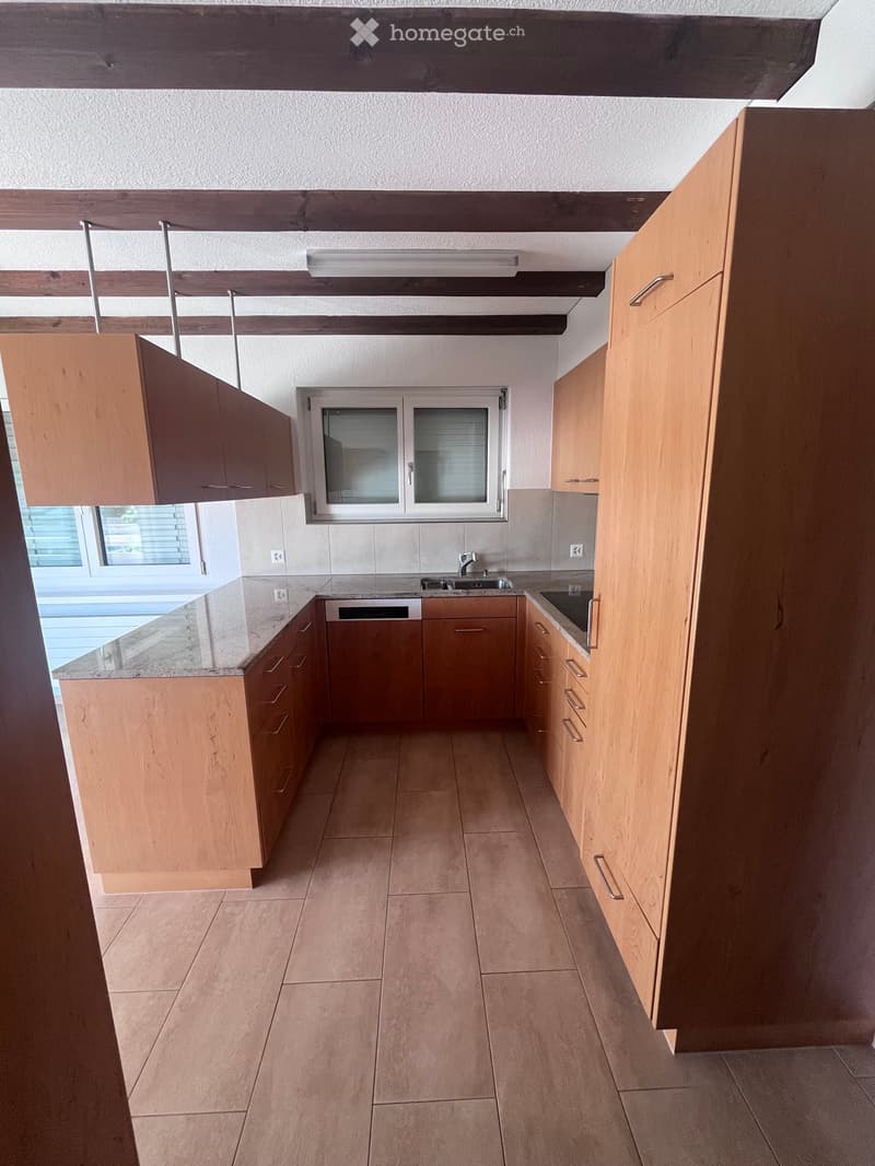 Modern kitchen with light wooden cabinets, granite countertops, and a stainless steel sink.