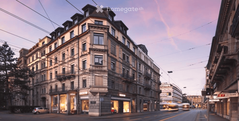 Multi-story urban building with classic architecture, large windows, and ground-floor storefronts. The building features ornate detailing and is situated on a street with visible traffic and surrounding structures.