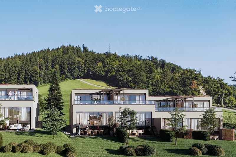 Modern residential complex with multiple buildings, large windows, balconies, and a spacious lawn area with outdoor seating and trees.