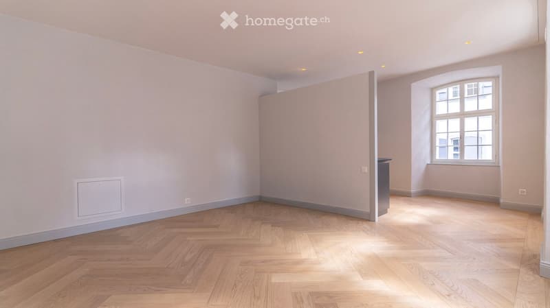 Empty room with light-colored walls, wooden floor, and a single window letting in natural light.