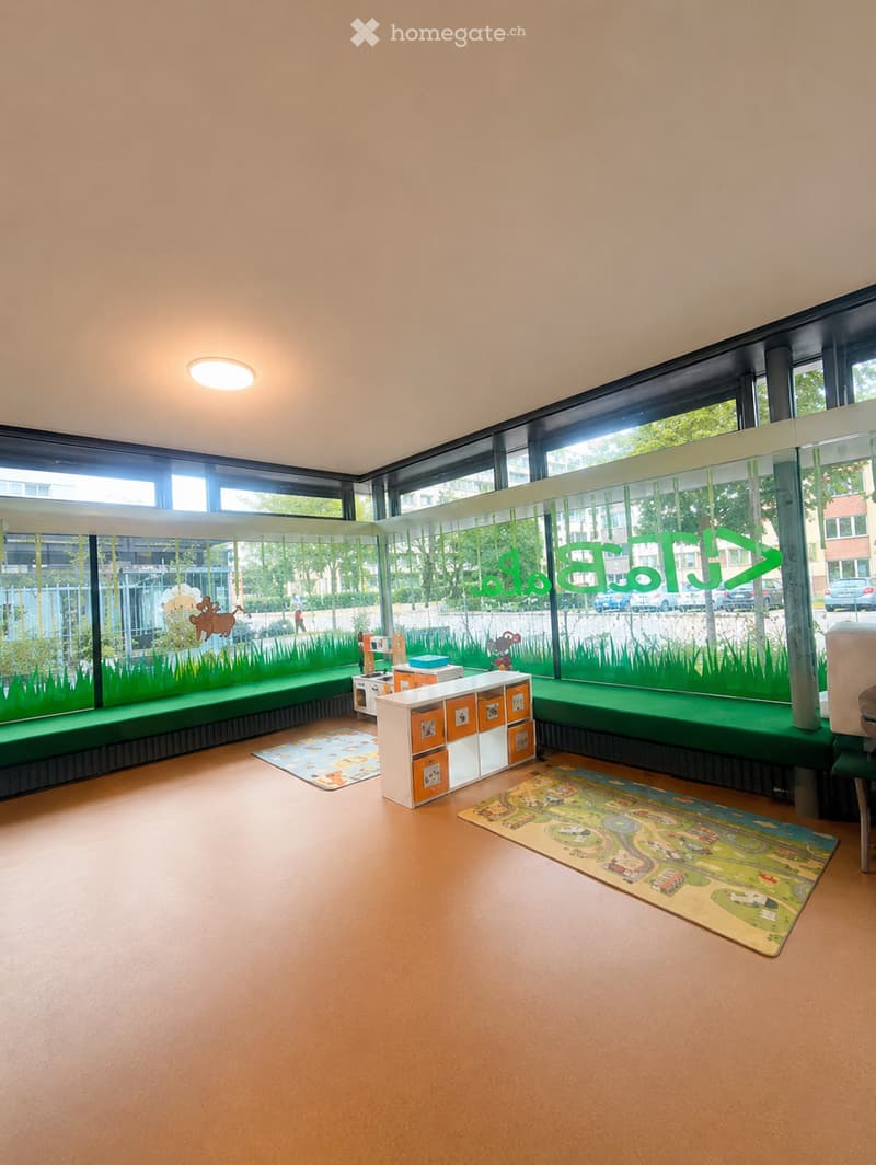 Bright, modern room with large windows, green bench seating, colorful play mats, and storage units.