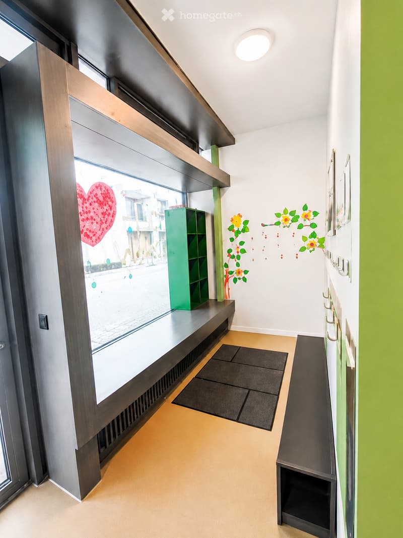 Modern hallway with large window, wooden floor, green shelving unit, decorative wall art, and coat hooks.