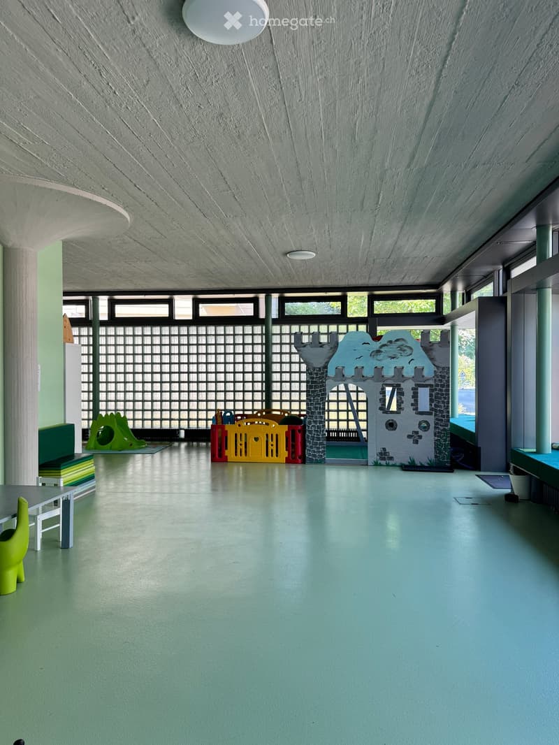 Brightly colored children's play area with a large toy castle, slide, colorful toy box, small table and chairs, and a green toy figure on the floor.