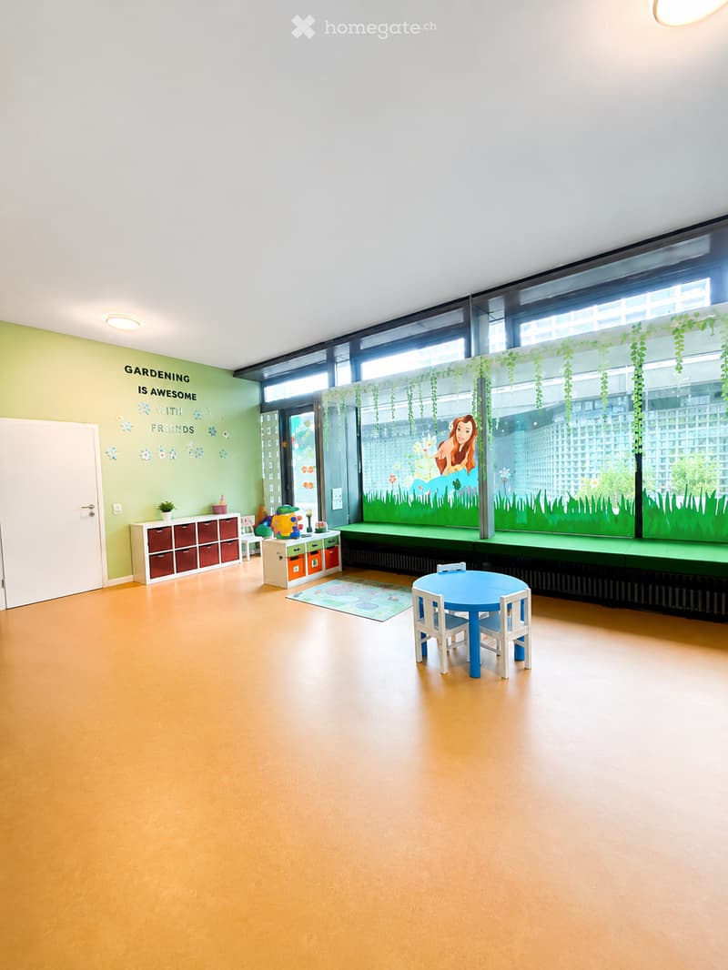 Bright, child-friendly room with a blue table and chairs, colorful storage units, a small plant, and a mural on the wall.