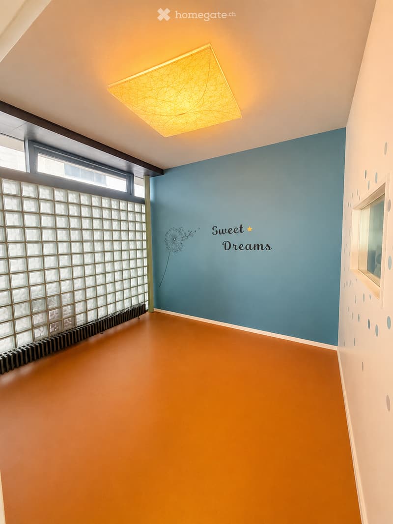 Empty room with orange flooring, blue accent wall, decorative dandelion design, and a modern geometric light fixture.