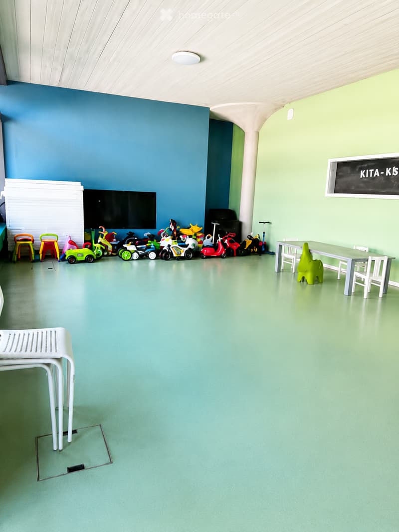 Brightly colored room with green floor, blue and green walls, a large screen, colorful toys, a table with chairs, and a stool.