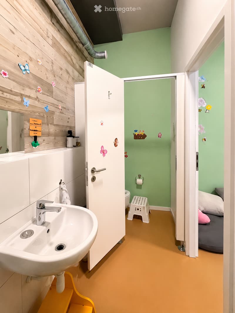 Bathroom with a white sink, mirror, and cabinet. A small white stool is placed near the toilet, and the walls are painted green with decorative stickers.