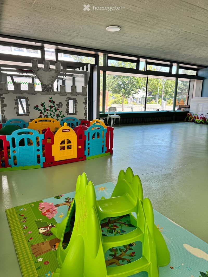 Brightly colored children's play area with toy castle, playhouse, toy cars, and chairs.