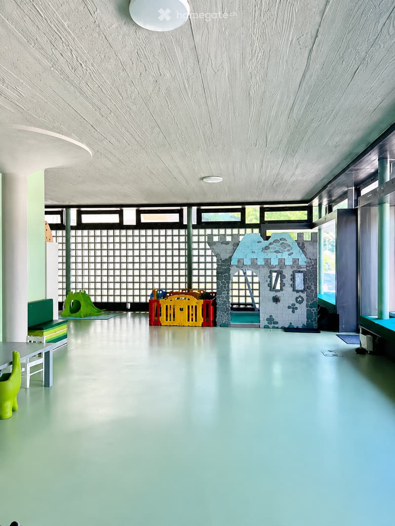 Bright, open play area with light blue floor, white ceiling, and colorful play structures including a toy castle, slide, and playhouse.