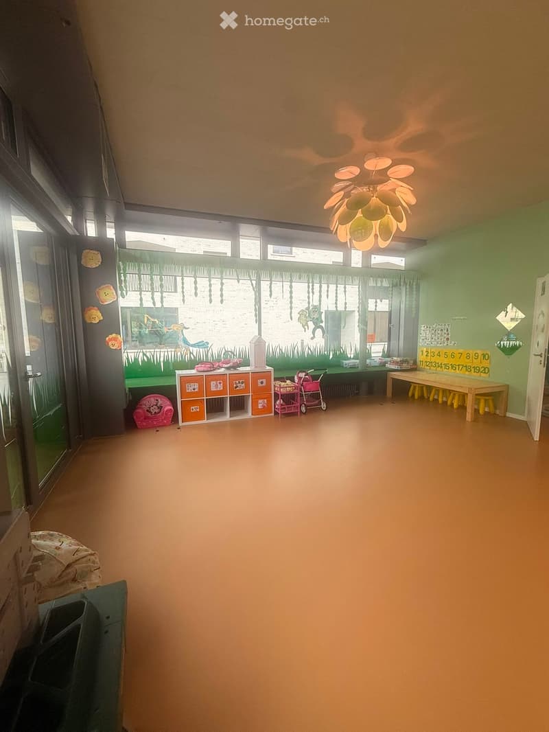 Brightly colored children's room with a green curtain, a table with stools, a storage unit, a toy stroller, and a toy chair.