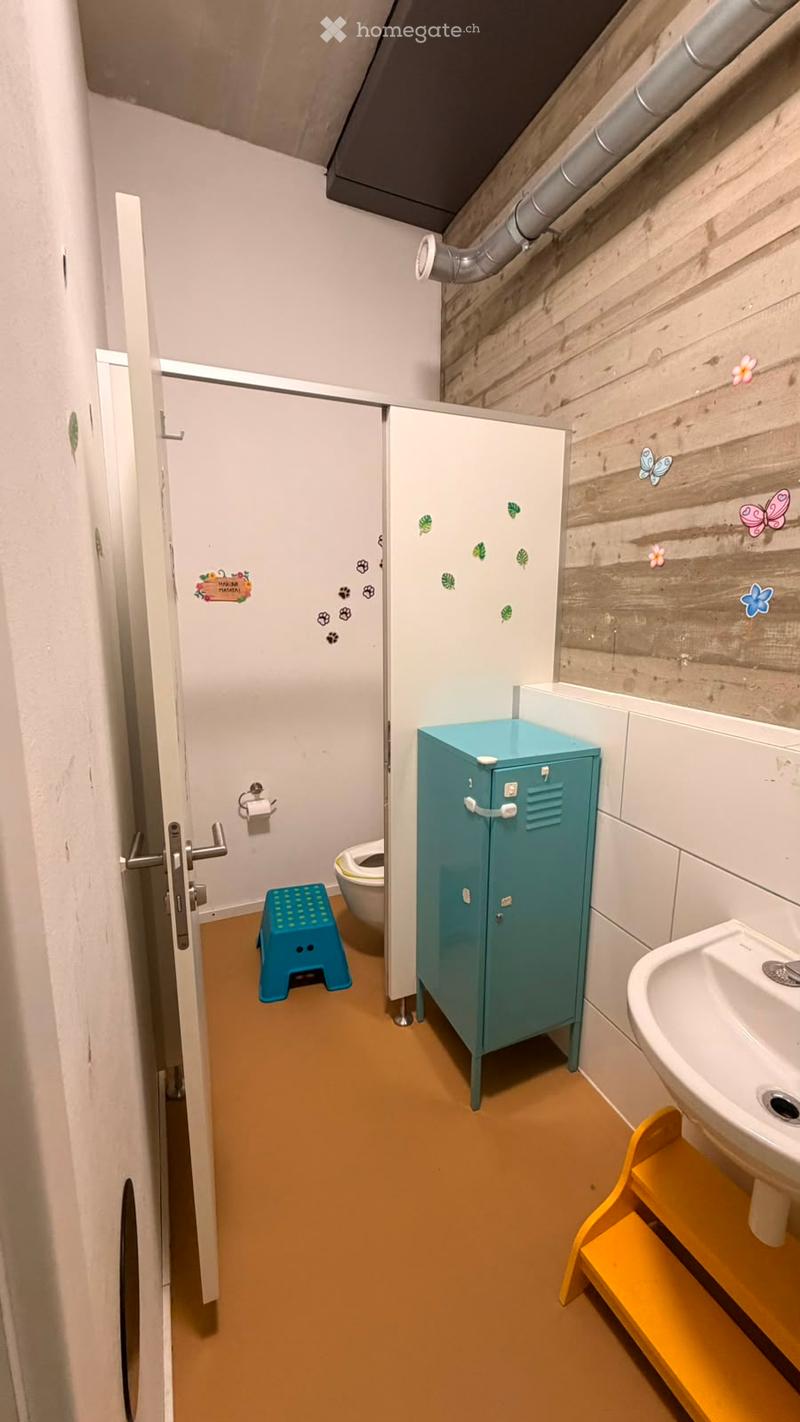 Bright, child-friendly bathroom with a sink, toilet, blue locker, and colorful stools for accessibility.