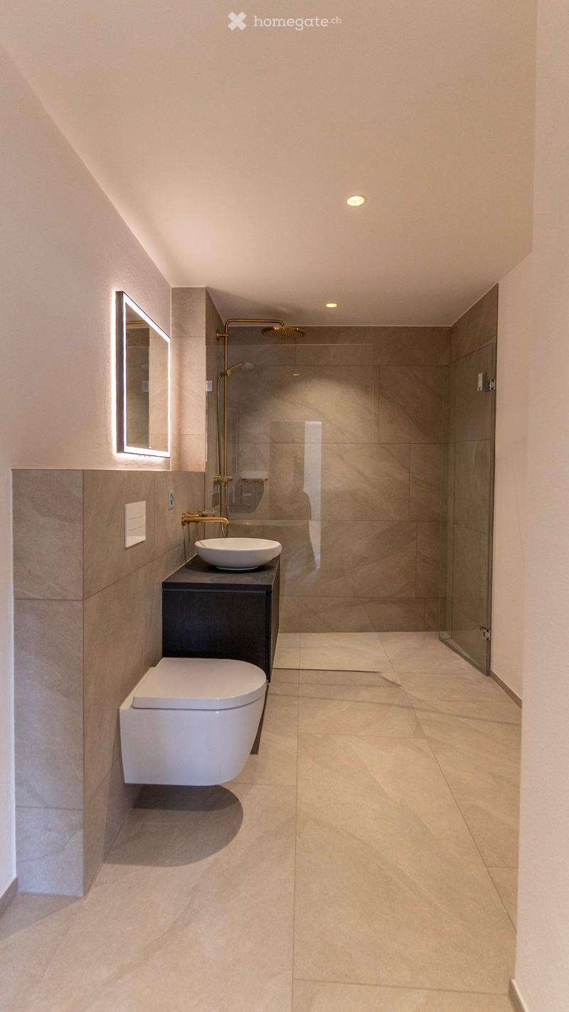 Modern bathroom with a toilet, sink, mirror, and glass-enclosed shower area. Light-colored tiles and sleek fixtures.