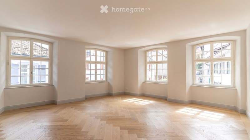 Empty room with light-colored walls and wooden flooring, featuring multiple large windows with white frames and frosted glass panes.