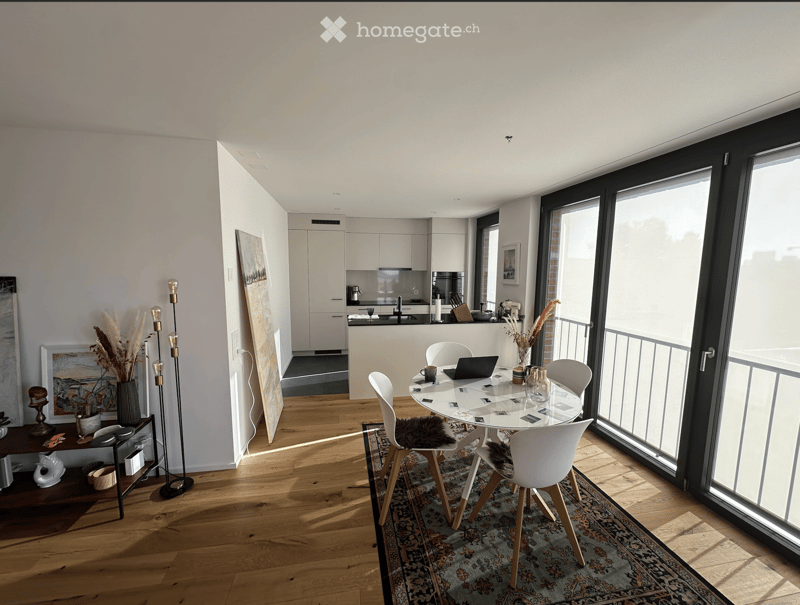 Open-plan living and dining area with modern furniture, large windows, and a sleek kitchen in the background.