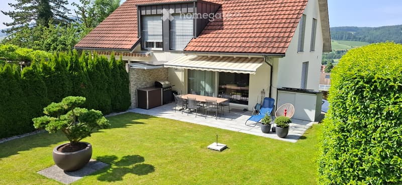 Well-maintained garden with a lawn, potted plants, outdoor dining set, and a covered patio area with a grill and seating.