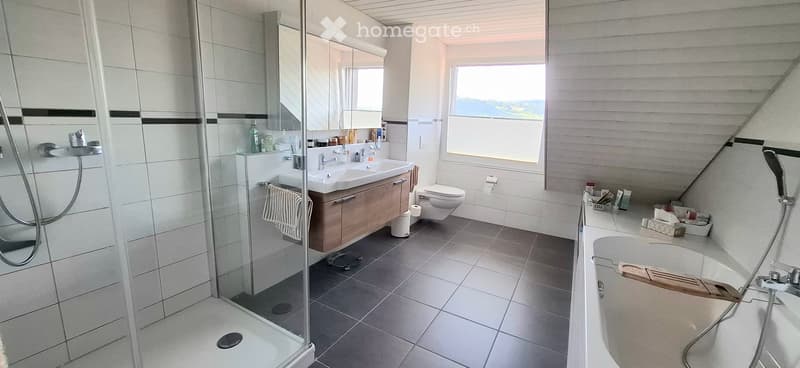 Modern bathroom with a bathtub, toilet, sink, mirror, and a glass-enclosed shower. The space features light-colored tiles and a wooden cabinet.