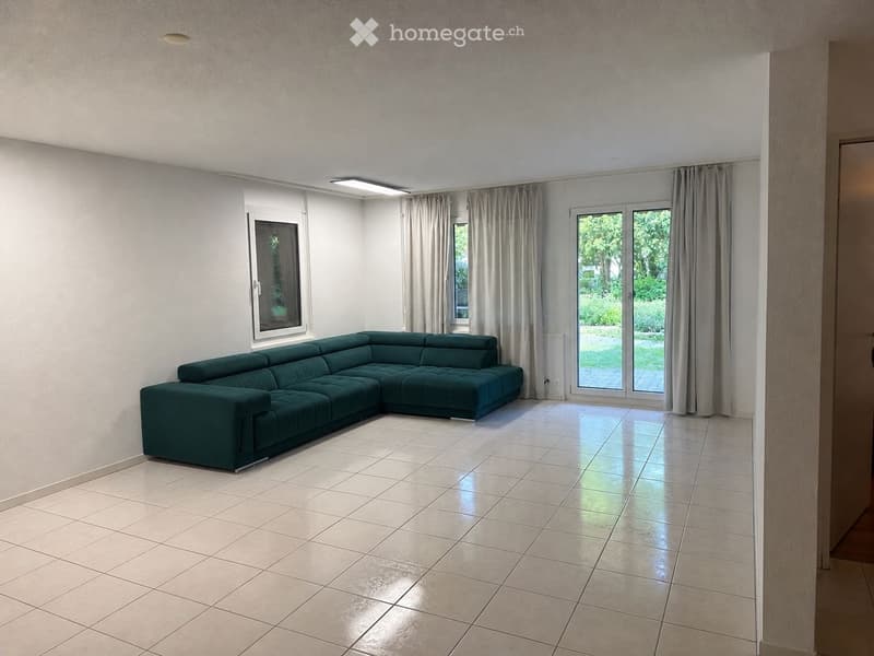 Modern living room with a green sectional sofa, large windows with curtains, and tiled flooring.