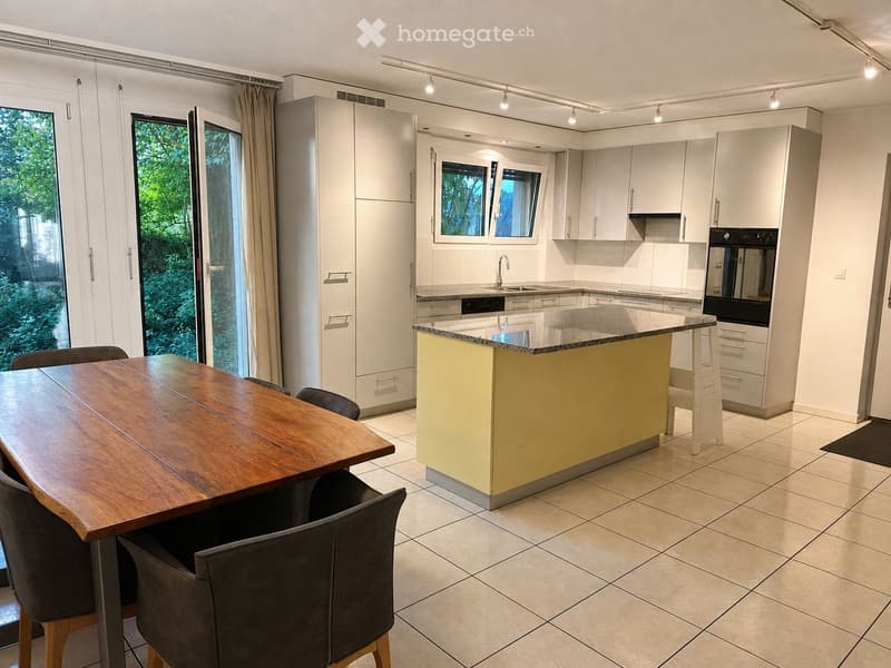 Modern kitchen with white cabinets, a central island, a sink, and a dining area with a wooden table and chairs.