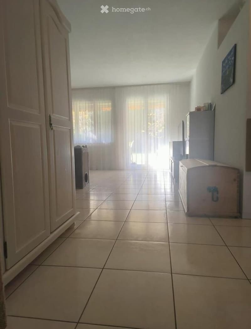 Empty hallway with tiled floor, white walls, and large window with sheer curtains at the end.